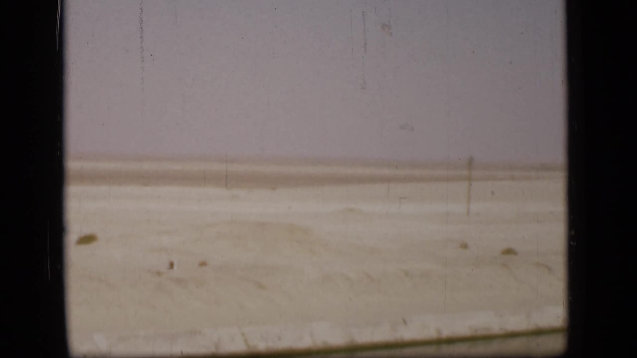 Open desert terrain in the Suez Canal region, with small dark marks on the sand, a pale horizon, and visible 8mm scratches.