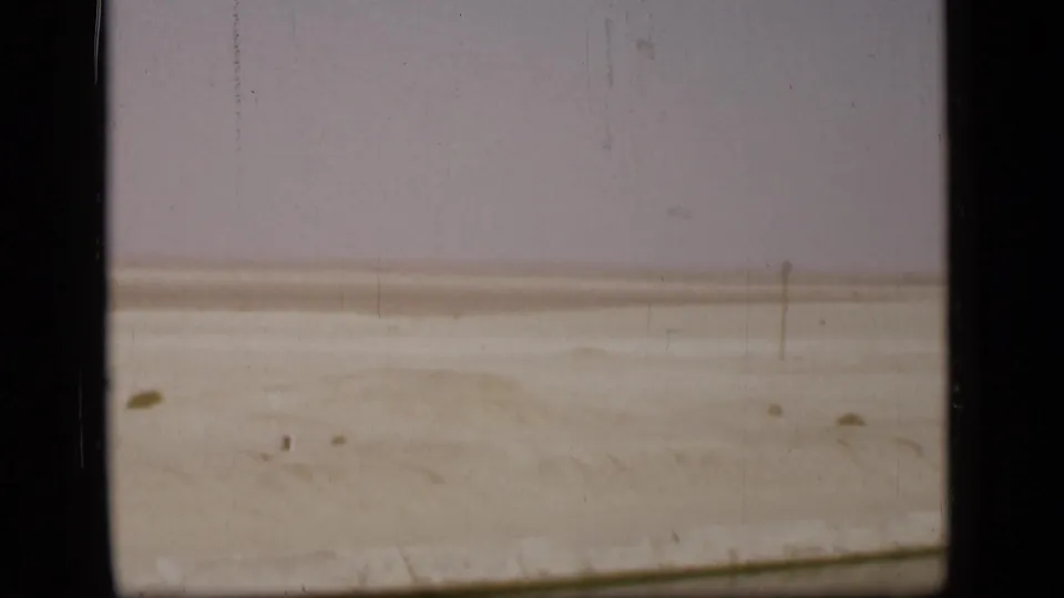 Open desert terrain in the Suez Canal region, with small dark marks on the sand, a pale horizon, and visible 8mm scratches.
