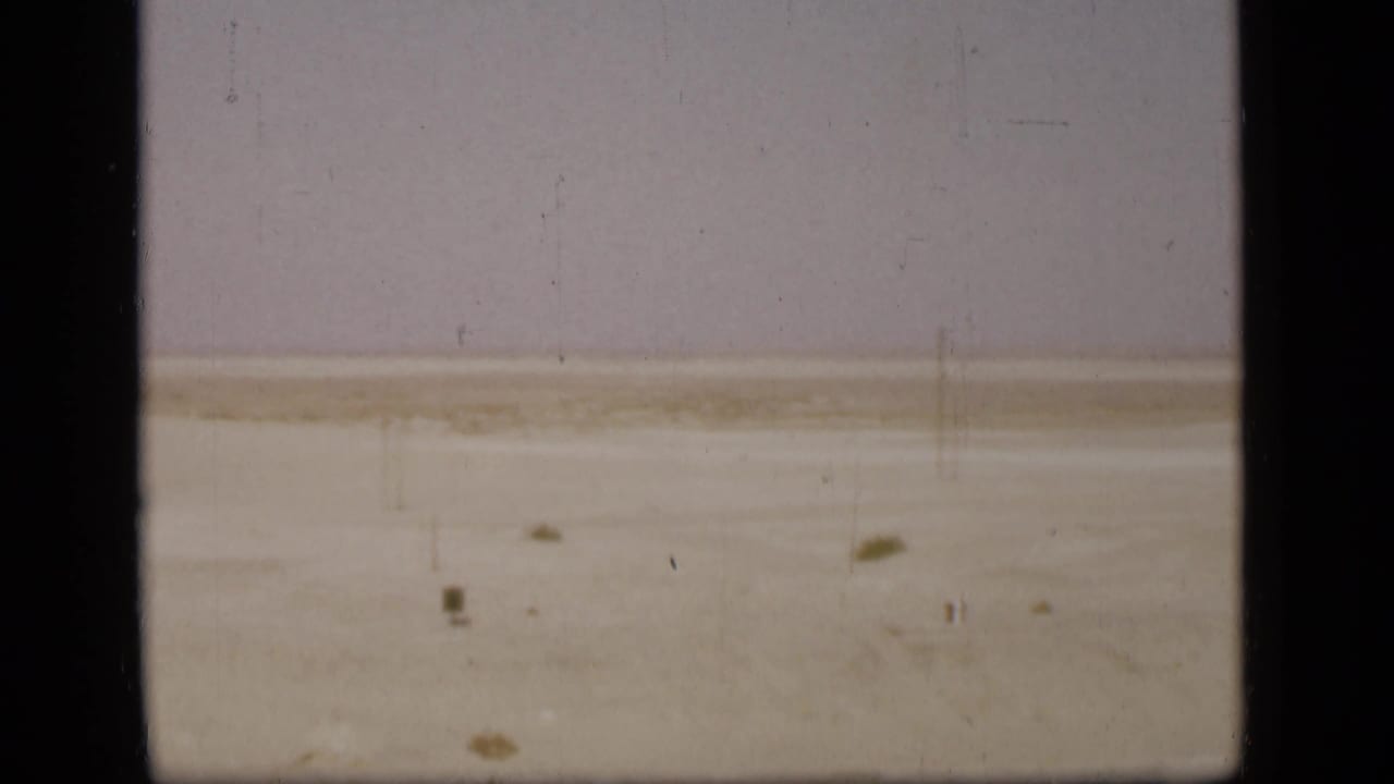 A muted 1946 8mm view of the Suez Canal area desert, showing flat sand, scattered scrub, and aged film wear.