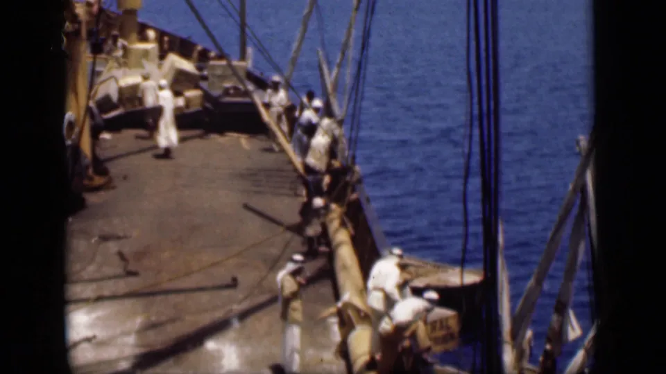 Mid-1940s Suez Canal home-movie frame of men on a sailing vessel deck, with rigging, deck gear, and blue water in view.