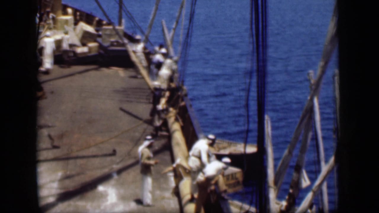 Suez Canal, Egypt, 1946 frame showing crew in white clothing near deck boxes, rigging, and a wooden boom with water beside the vessel.