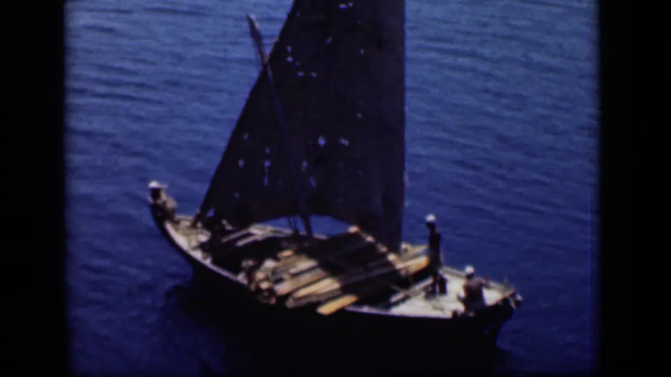 A small wooden sailboat with a dark triangular sail carries people and goods on blue Suez Canal water in 1946 footage.