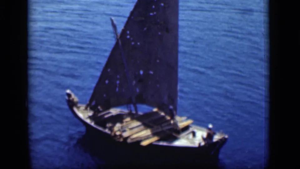 A small wooden sailboat with people aboard and a dark triangular sail moves through the Suez Canal in 1946 8mm footage.