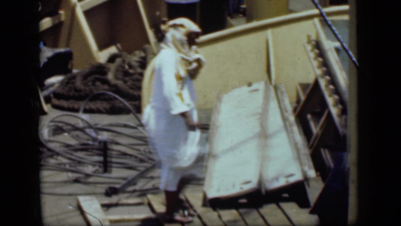 A man in white robes and headscarf walks along a working dock area in 1946 Suez Canal footage.