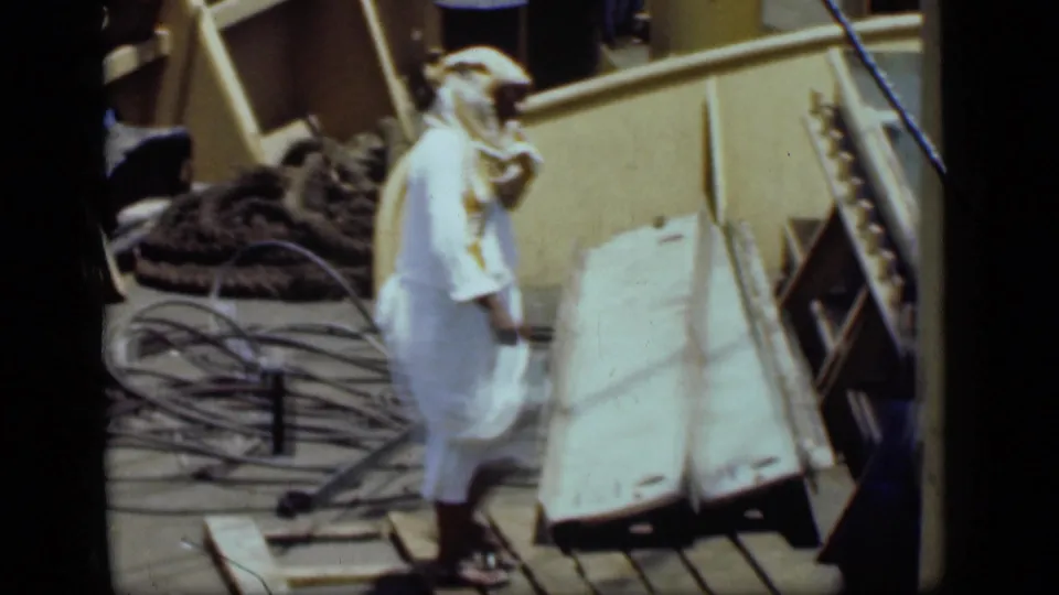 A man in white robes and headscarf walks along a working dock area in 1946 Suez Canal footage.