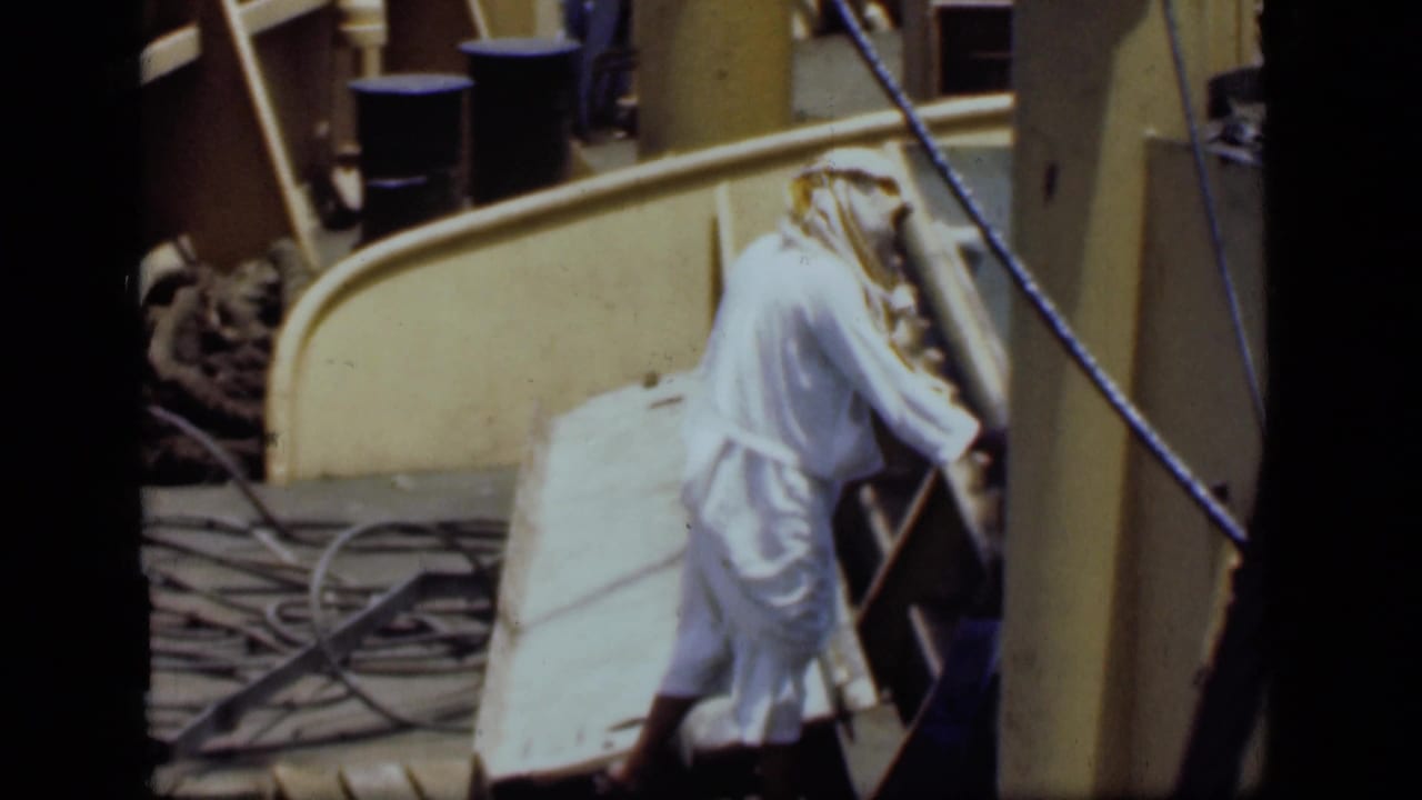 A robed man stands near railings, ropes, and dock equipment in the Suez Canal port setting.