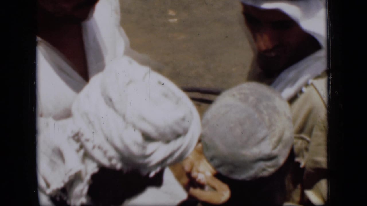 1946 Suez Canal frame showing men in white head coverings clustered over hands and a small object, suggesting counting or inspection.