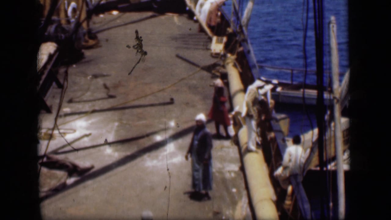1946 Suez Canal home-movie frame showing men on a pier beside blue water, ropes, and a moored boat.