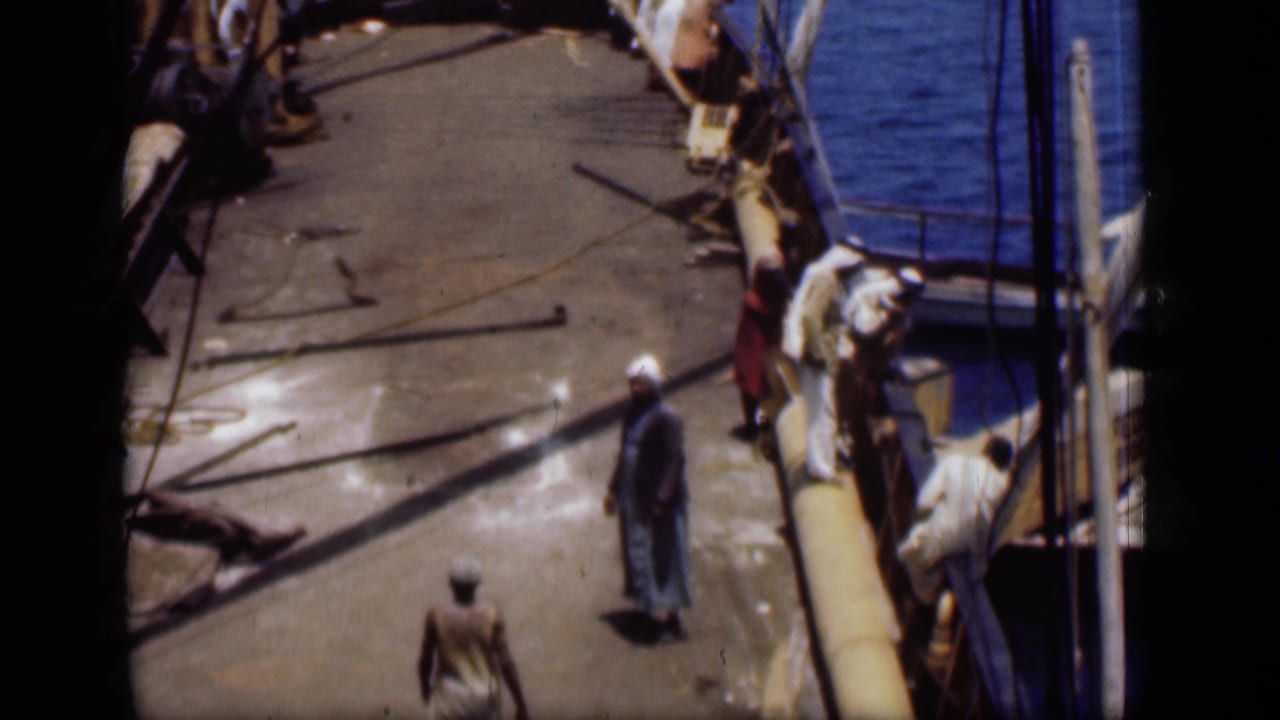 1946 Suez Canal frame with men moving and standing on a pier next to ropes, rigging, and blue water.