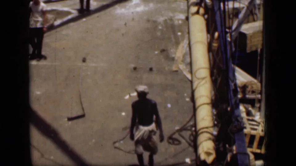 In 1946 Suez Canal footage, a man in a white headwrap and light cloth walks across a sunlit boat deck.