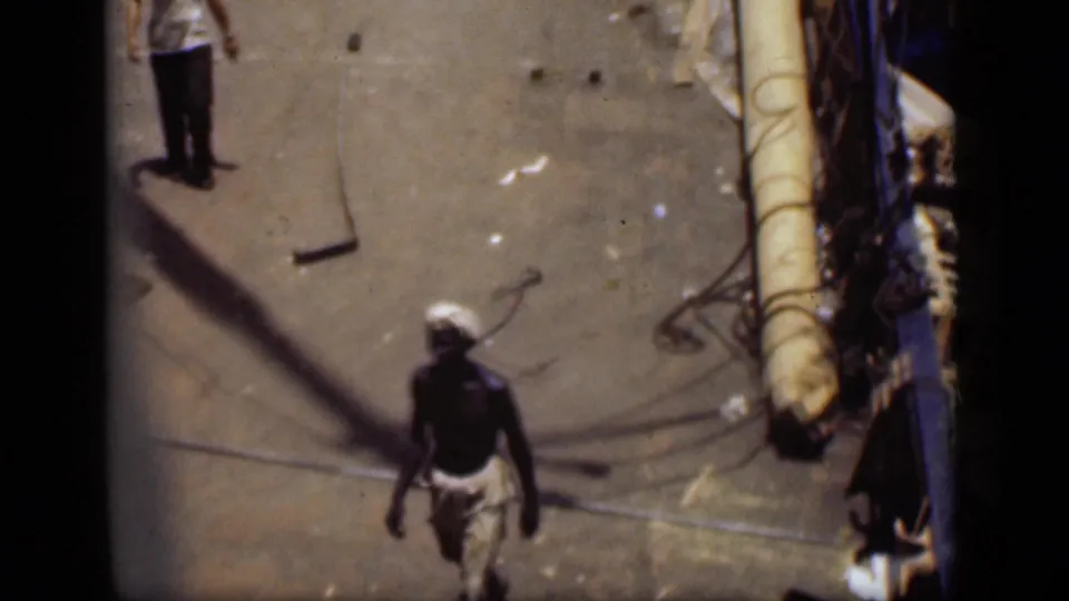 A man in a white headwrap moves along the deck of a boat in Suez Canal home-movie footage from 1946.