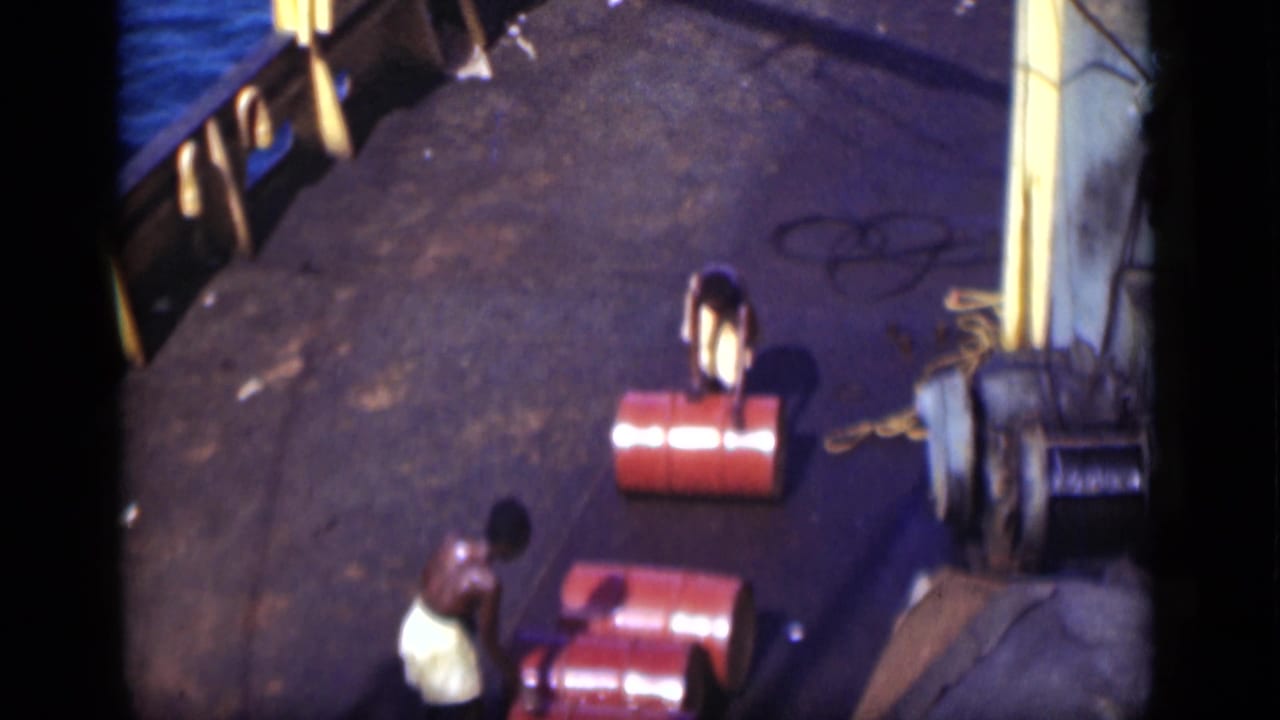High-angle 1946 Suez Canal deck view with two shirtless men handling red barrels near railings and rope.