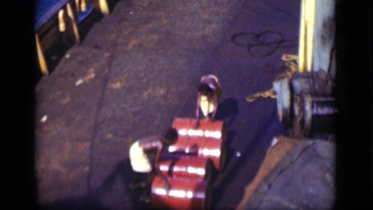Two men on a 1946 Suez Canal vessel deck bend near bright red barrels, with rope and railings visible.