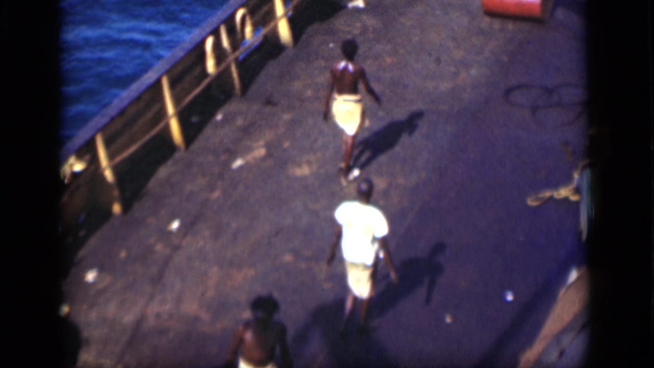Two men walking on a ship deck beside blue water and yellow railings.