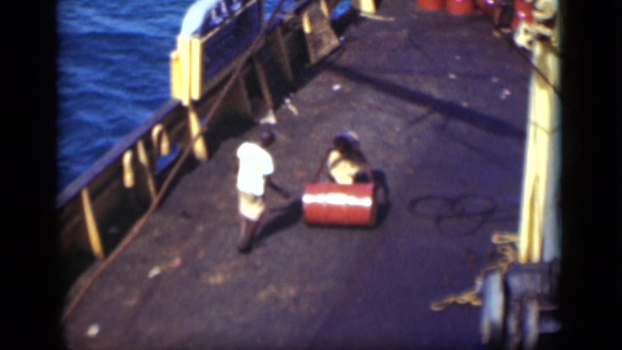 1946 Suez Canal footage shows two men beside a red barrel on a ship deck with yellow railings and canal water.