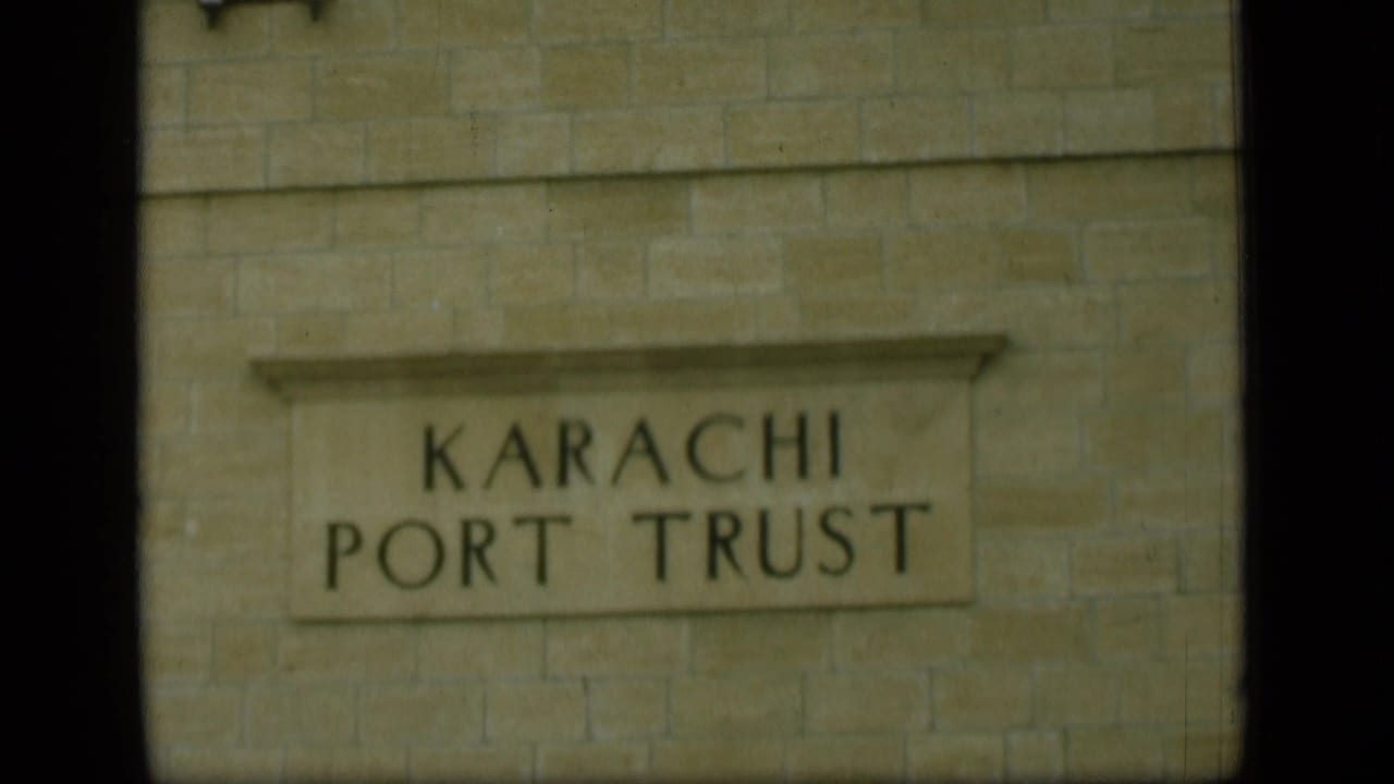 The 8mm frame shows a closer, slightly soft view of the Karachi Port Trust sign set into a stone wall.