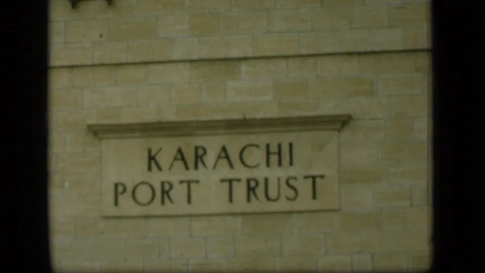 The final frame holds on the Karachi Port Trust sign, with dark frame edges and soft 8mm color.
