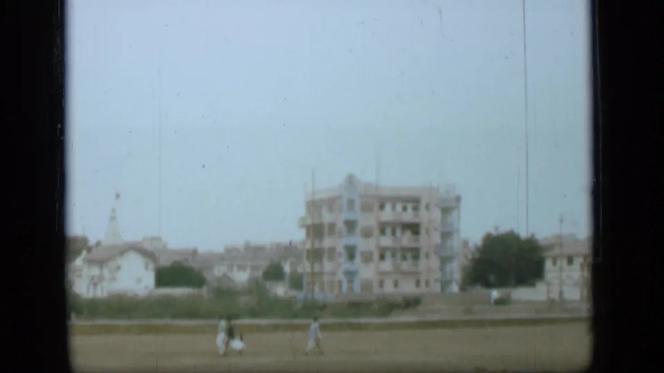 1946 8mm home-movie view associated with Suez Canal metadata, showing distant pedestrians crossing grass near low walls and urban buildings.
