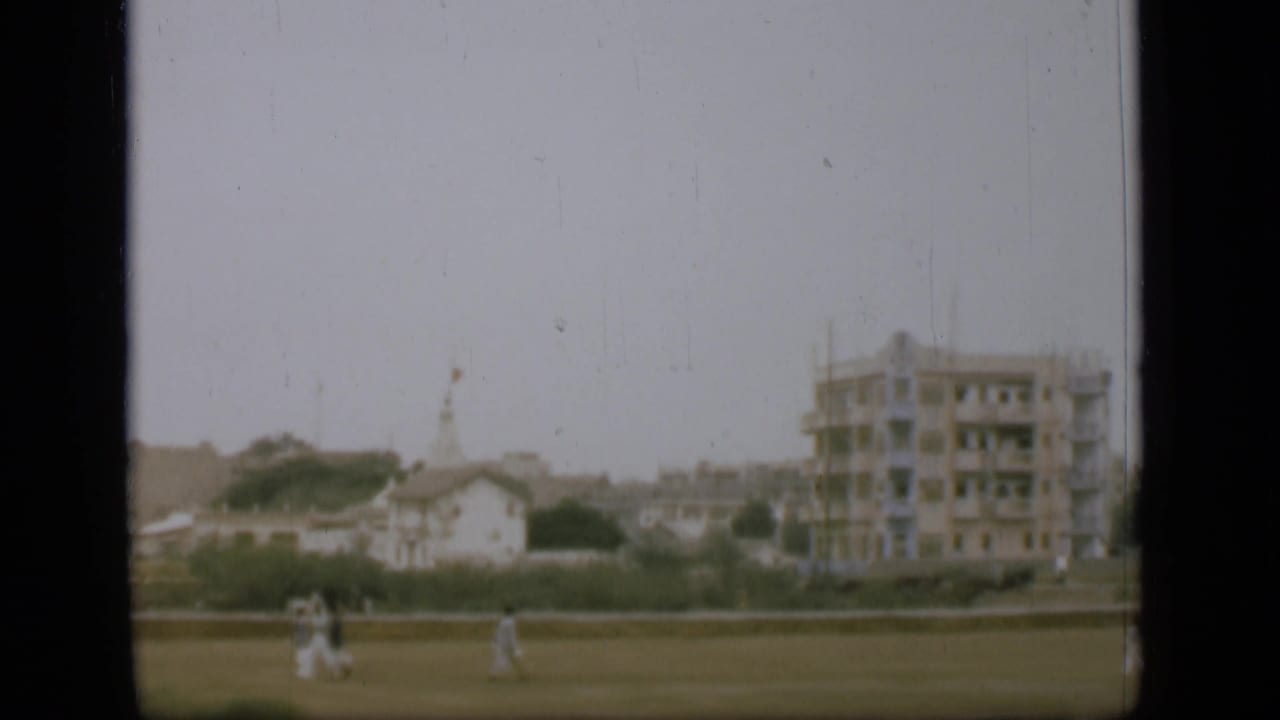 1946 8mm view near the Suez Canal area with distant people on open ground, low buildings, and a larger unfinished-looking structure.