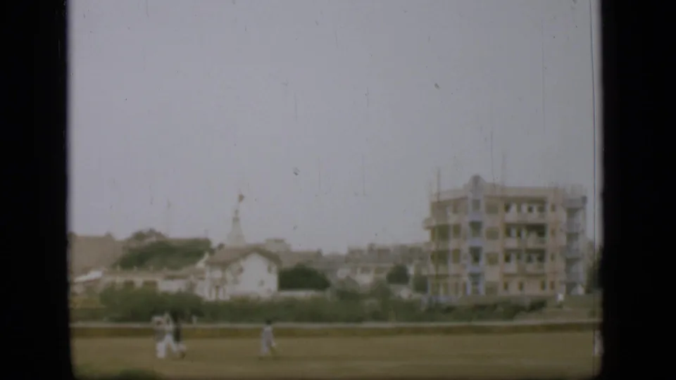 1946 8mm view near the Suez Canal area with distant people on open ground, low buildings, and a larger unfinished-looking structure.