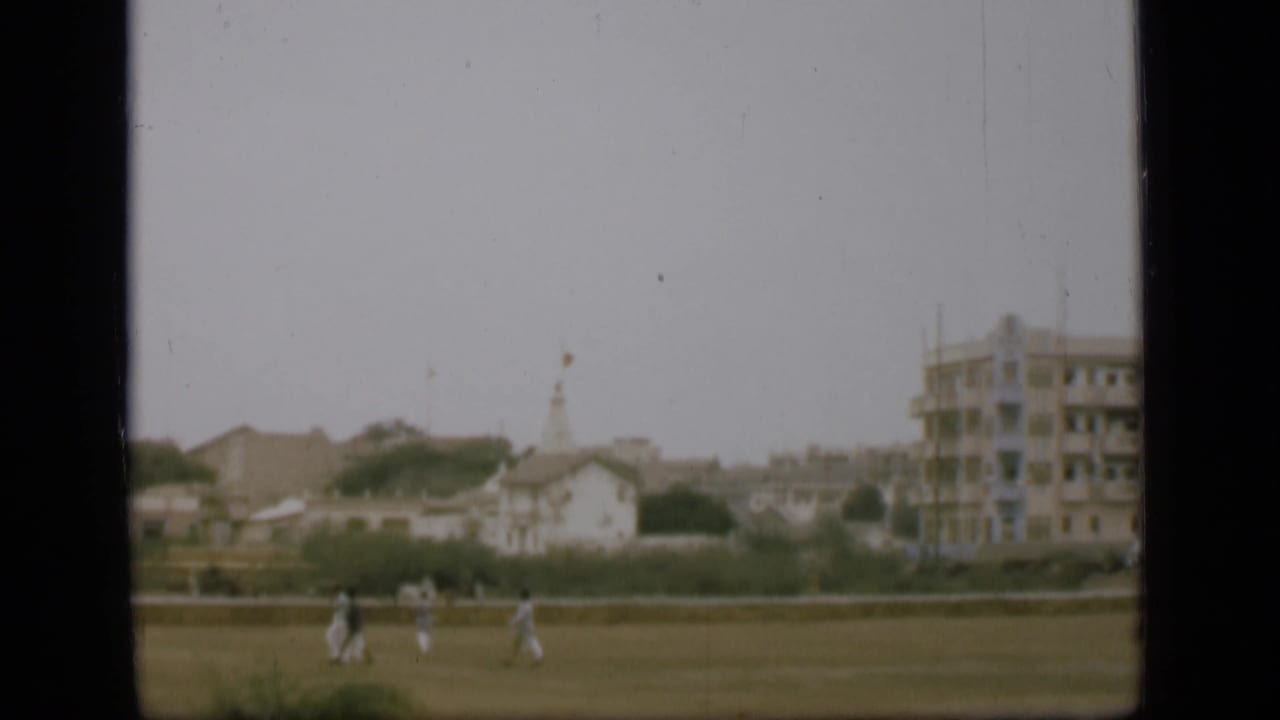 Distant 1946 Egypt home-movie frame showing people moving across open ground near low buildings and a larger structure.