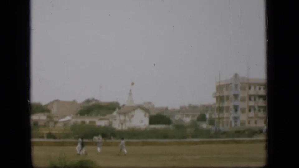 Distant 1946 Egypt home-movie frame showing people moving across open ground near low buildings and a larger structure.