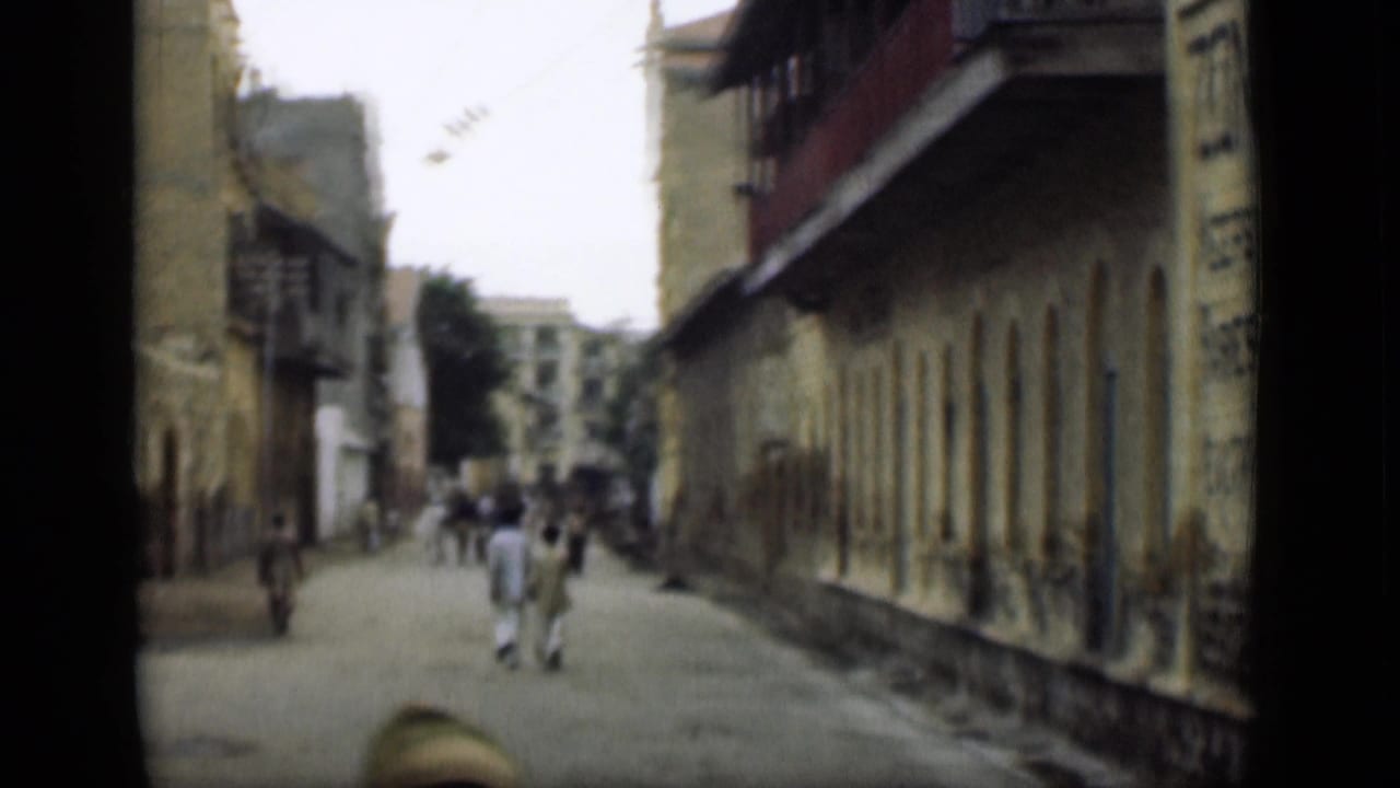 A narrow street in the stated Suez Canal, Egypt footage shows pedestrians walking between older multi-story buildings with balconies and worn facades.