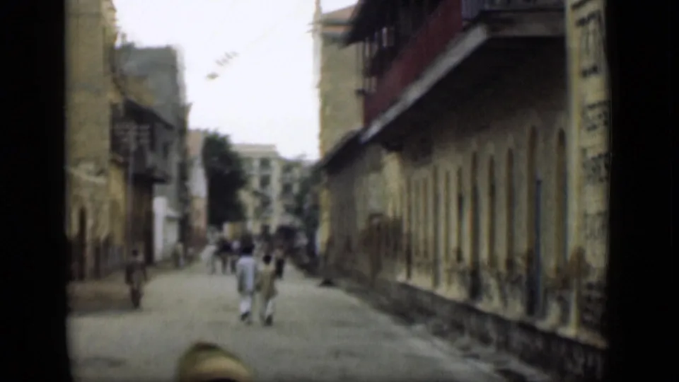 A narrow street in the stated Suez Canal, Egypt footage shows pedestrians walking between older multi-story buildings with balconies and worn facades.