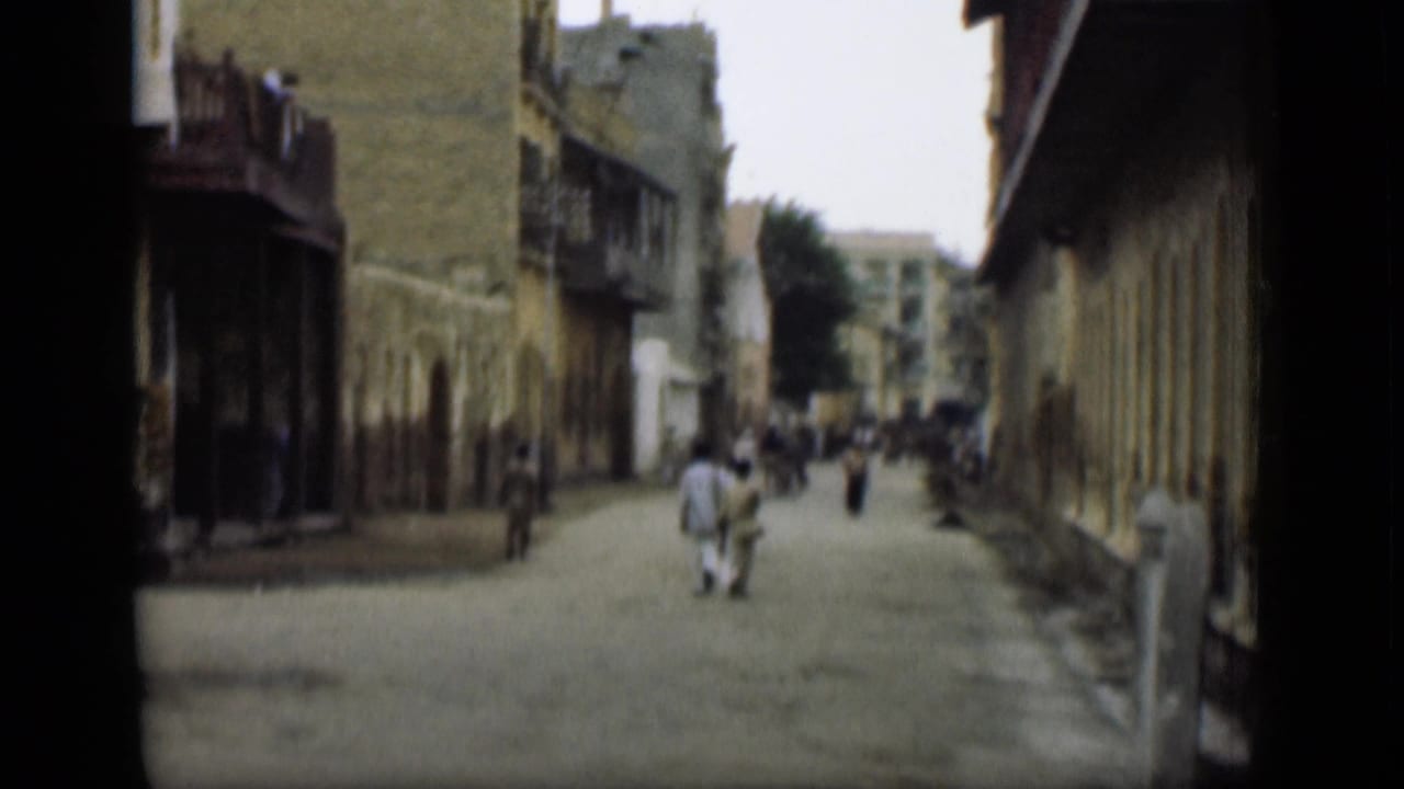 The camera looks down a quiet street in the stated 1946 Egypt footage, with pedestrians, balconies, and long building facades visible.