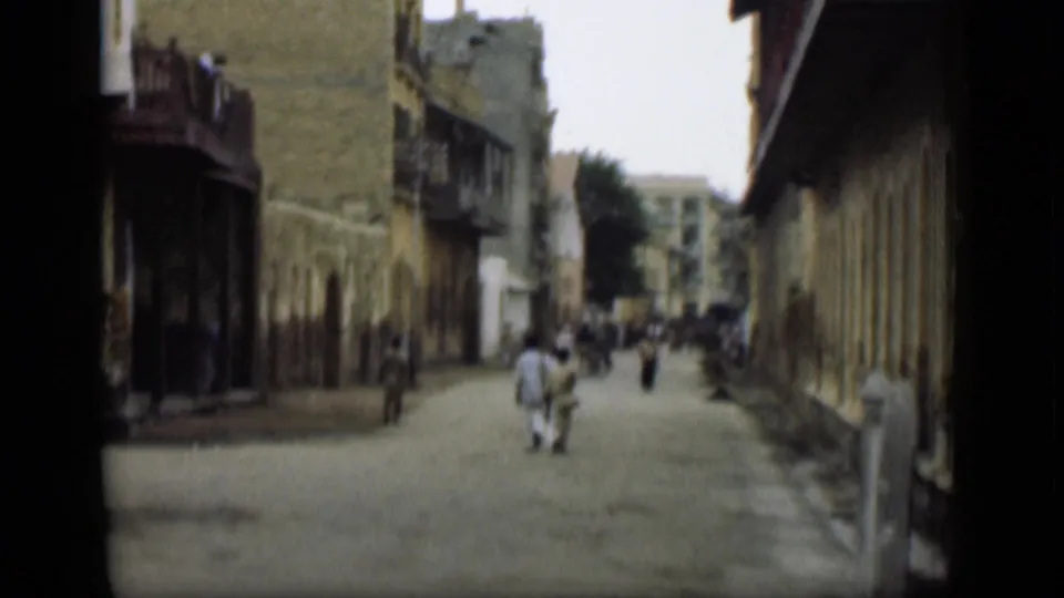 The camera looks down a quiet street in the stated 1946 Egypt footage, with pedestrians, balconies, and long building facades visible.