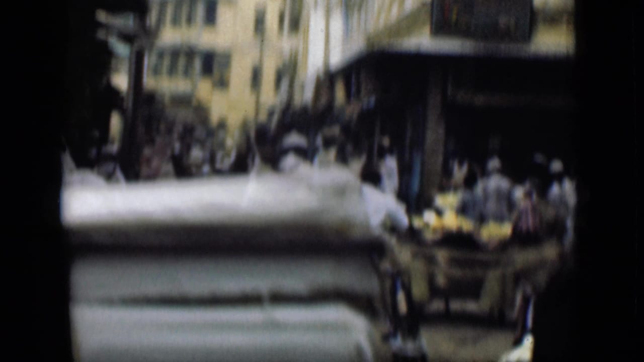 Blurred market street with pedestrians, awnings, pale buildings, and a cart or tray of goods in the foreground.