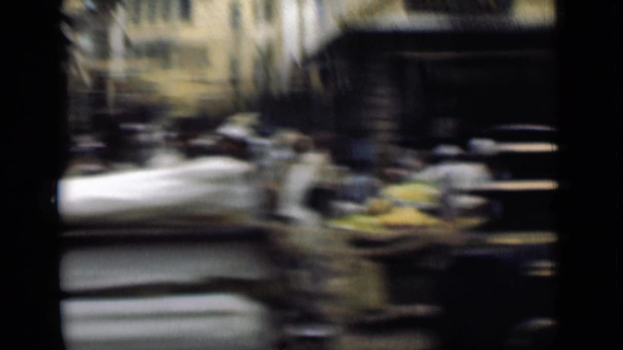 Motion-blurred 1946 Suez Canal, Egypt street frame with pedestrians, shaded storefronts, pale buildings, and goods or carts along the road.