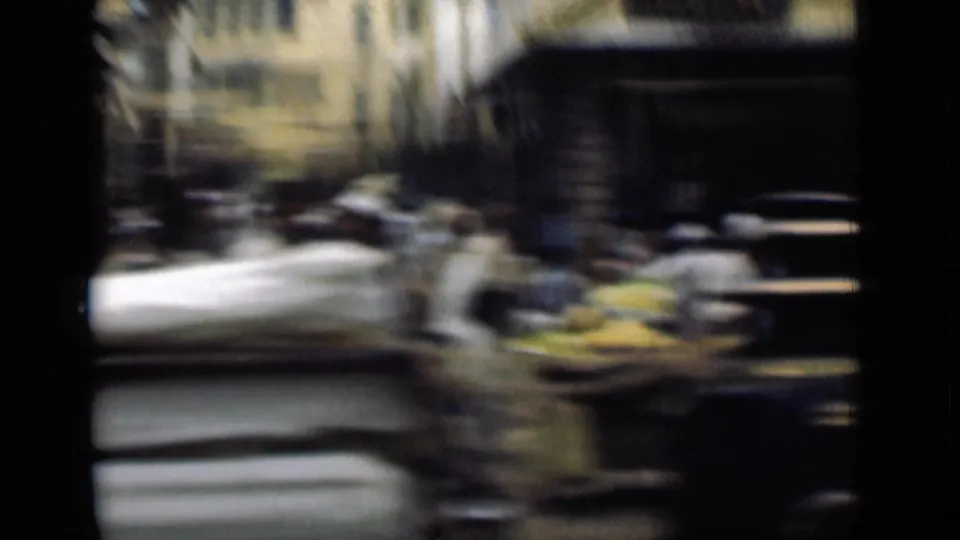 Motion-blurred 1946 Suez Canal, Egypt street frame with pedestrians, shaded storefronts, pale buildings, and goods or carts along the road.