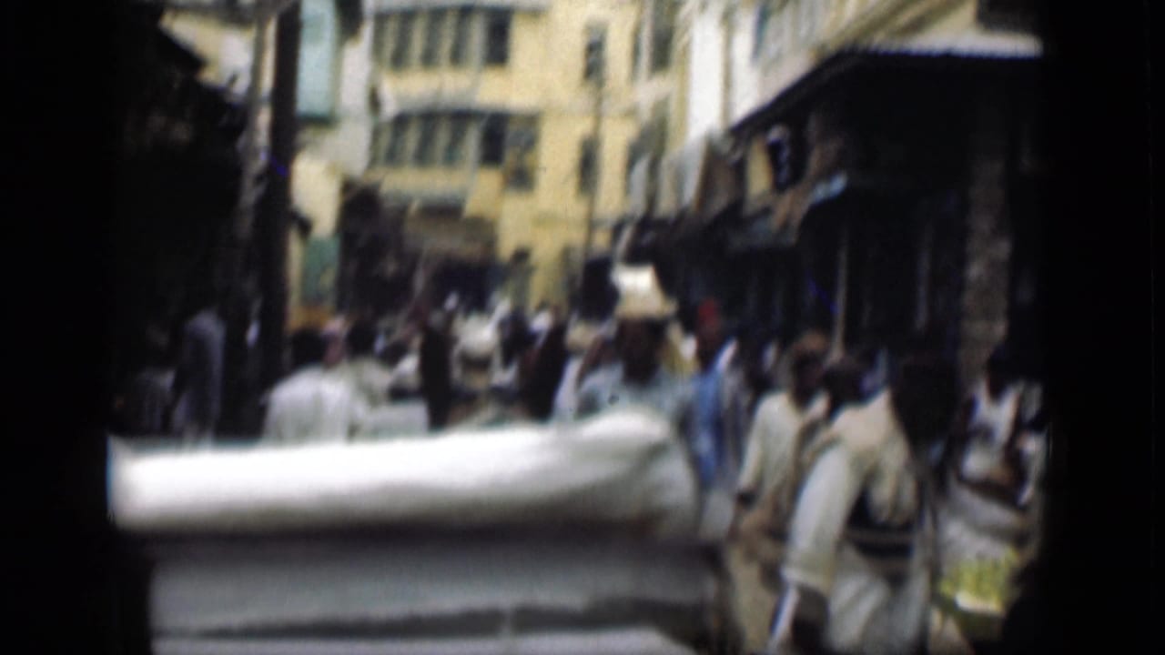 1946 Suez Canal region street scene with pedestrians passing shopfronts and awnings in a crowded market lane.