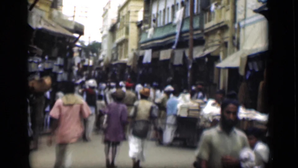 Handheld 8mm frame of a crowded Suez Canal region market street with carts, pedestrians, and shaded storefronts.