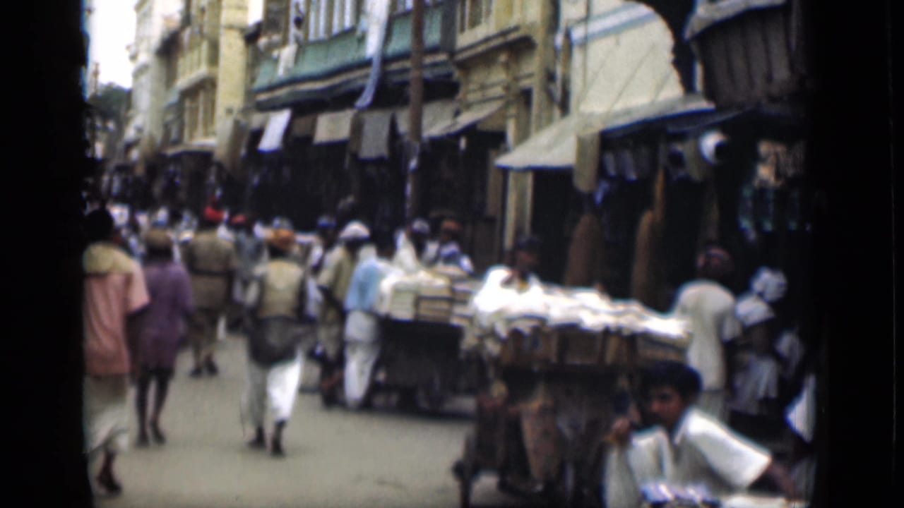 1946 Suez Canal region market lane with pedestrians moving among carts and stalls beneath shop awnings.