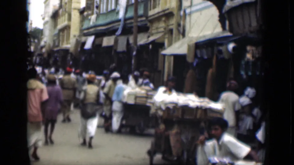 1946 Suez Canal region market lane with pedestrians moving among carts and stalls beneath shop awnings.