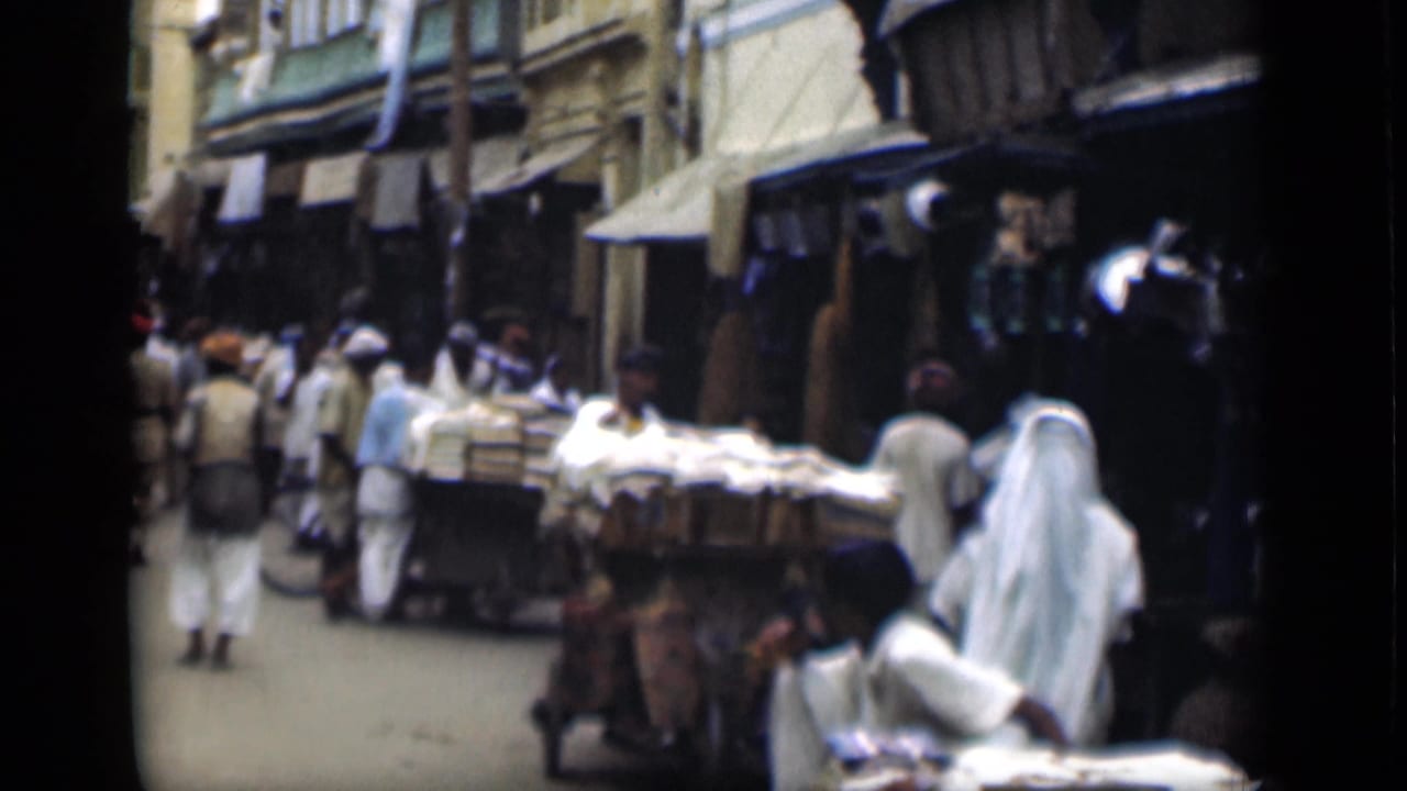 1946 Suez Canal region street-market view with pedestrians in light clothing, shop awnings, and a cart loaded with goods.