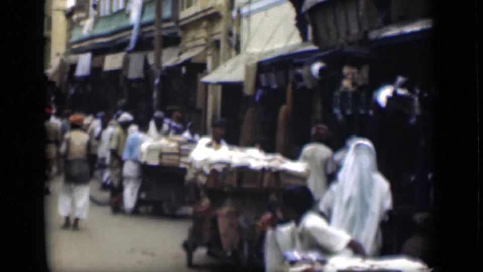 1946 Suez Canal region street-market view with pedestrians in light clothing, shop awnings, and a cart loaded with goods.