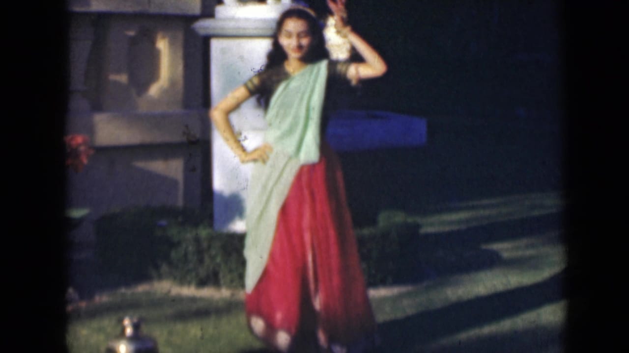 Young woman smiles while dancing in a garden, one hand raised and one hand on her hip.