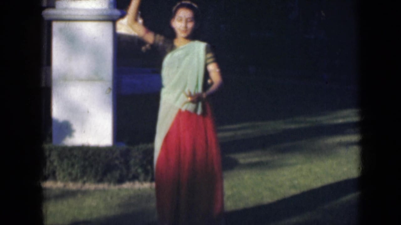 Young woman in a sari raises one arm while dancing on a sunlit lawn.