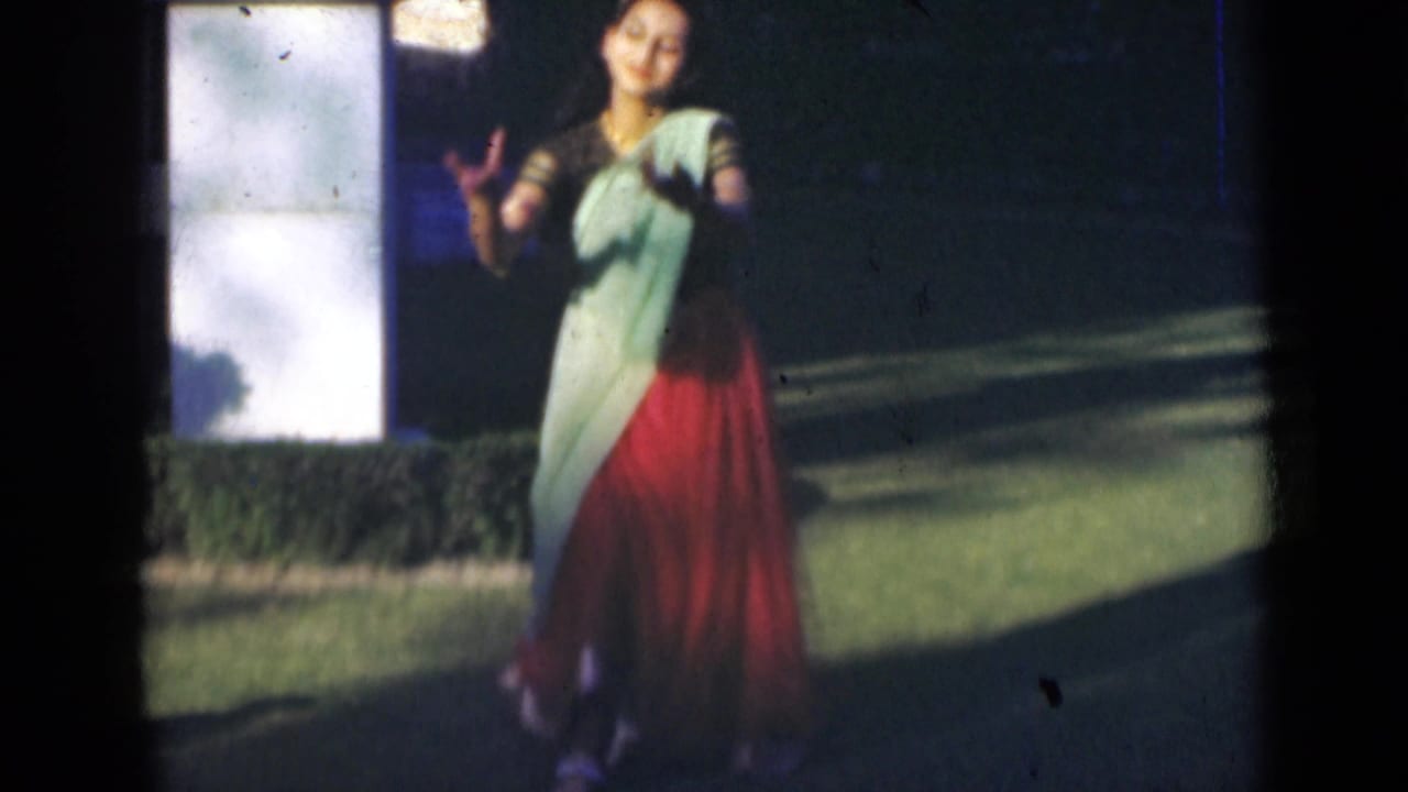 Woman in a sari dances on a lawn beside a white pillar.