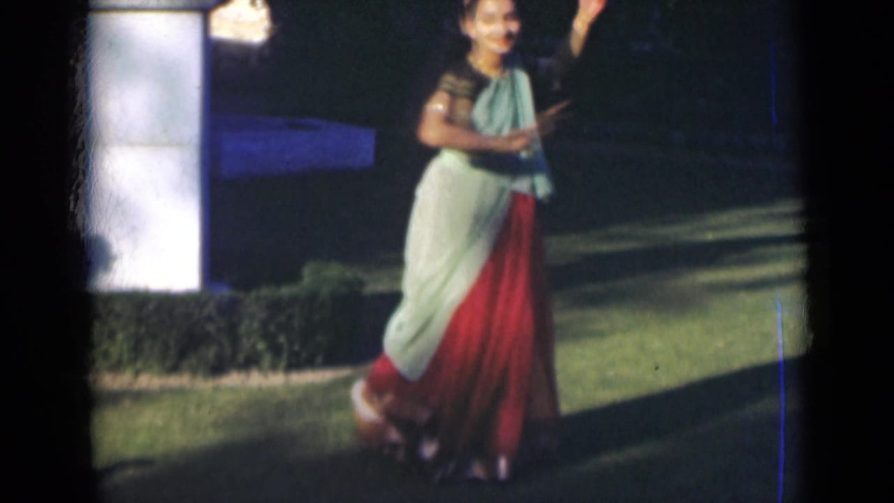 A smiling woman in a sari raises one arm during an outdoor dance pose in the 1947 India home-movie clip.