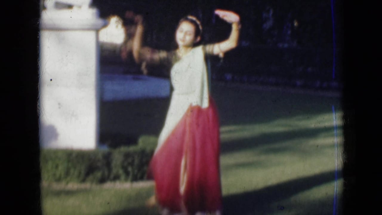 A 1947 India 8mm frame shows the woman extending one arm upward in a dance pose near a white column, hedge, and lawn.