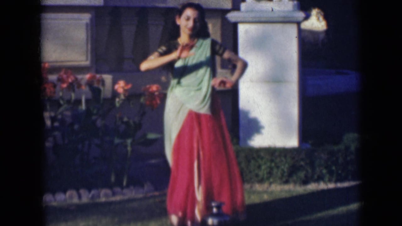 Woman in a sari performs a dance gesture with one hand across her chest.