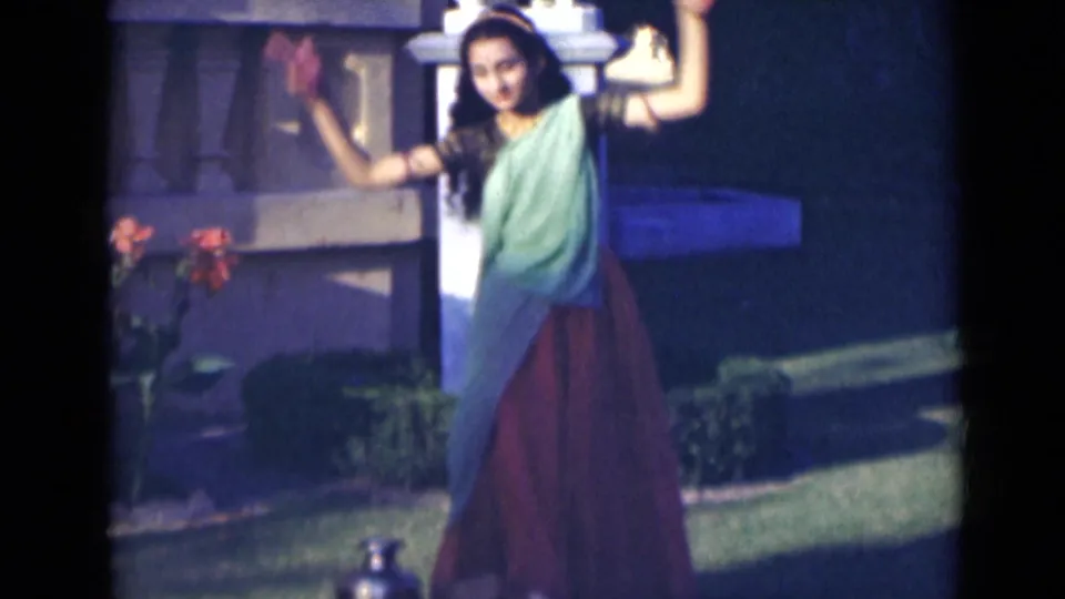 The dancer appears closer to the camera, raising both arms as the 8mm footage records her movement in a garden.
