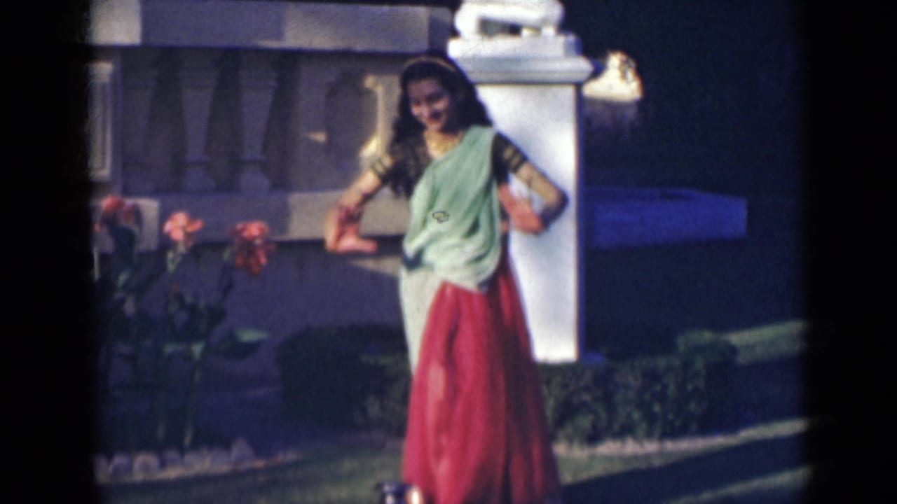 Woman in a sari lowering her hands toward a small vessel in the garden.