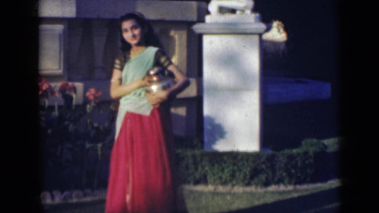 Young woman smiles while holding a metal vessel near a white pillar and garden plants.