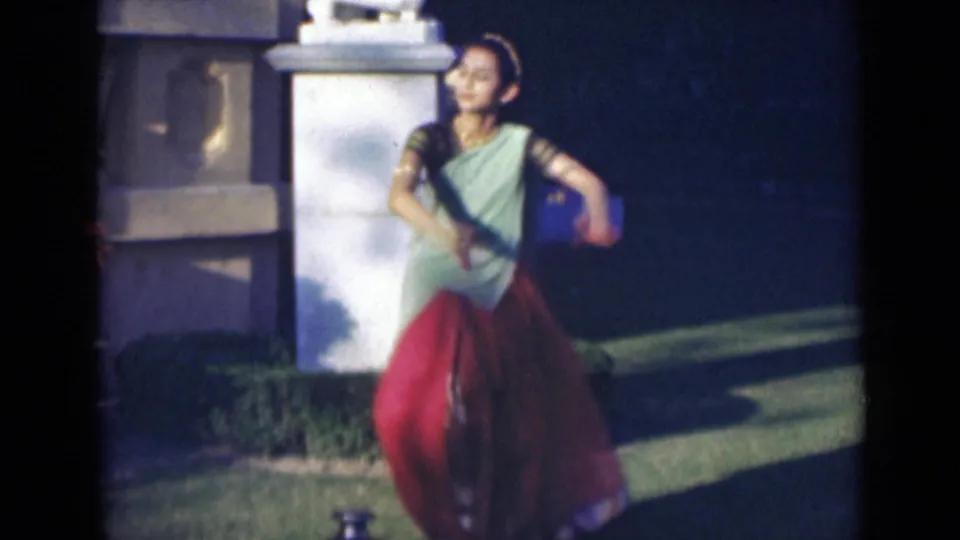In the final frame, the woman stands on the lawn in a green and red sari with the gold-colored jug visible near her feet.