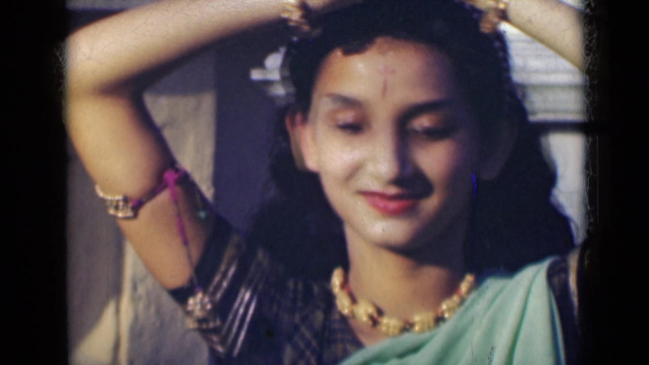 Young woman in a green sari raises her arms while facing the camera.